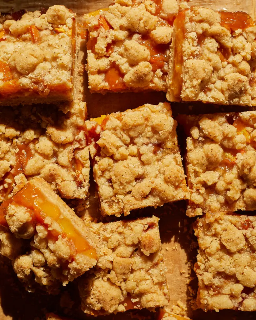 several slices of peach bars with brown butter crumble laid next to each other, one leans on top of the rest showing the fruit inside.