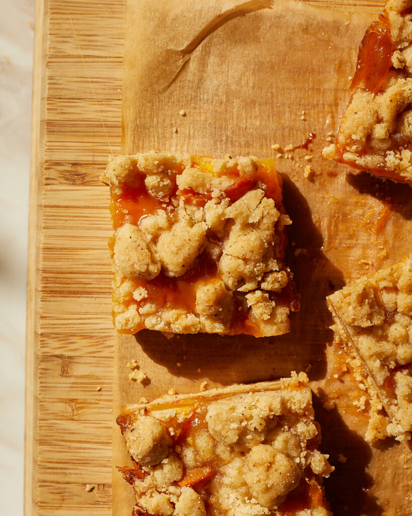 A square of peach bars with brown butter crumble on a wood cutting board