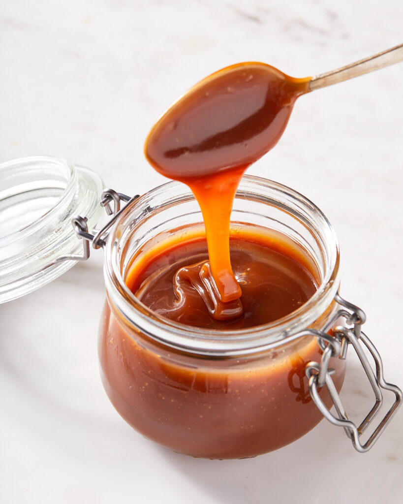 a spoon drizzling salted caramel sauce in a large  jar