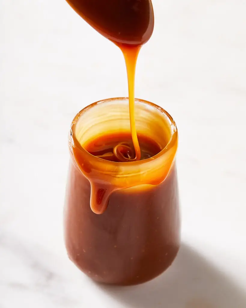 a spoon drizzling salted caramel sauce in a small  jar