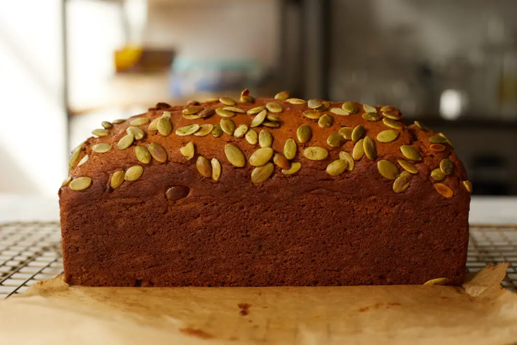 the side of a loaf of pumpkin bread on a cooling rack with pumpkin seeds or pepitas on top 