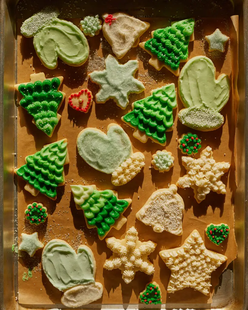 holiday sugar cookies like snowflakes, mittens, trees, stars and more, frosted with buttercream on a sheet tray
