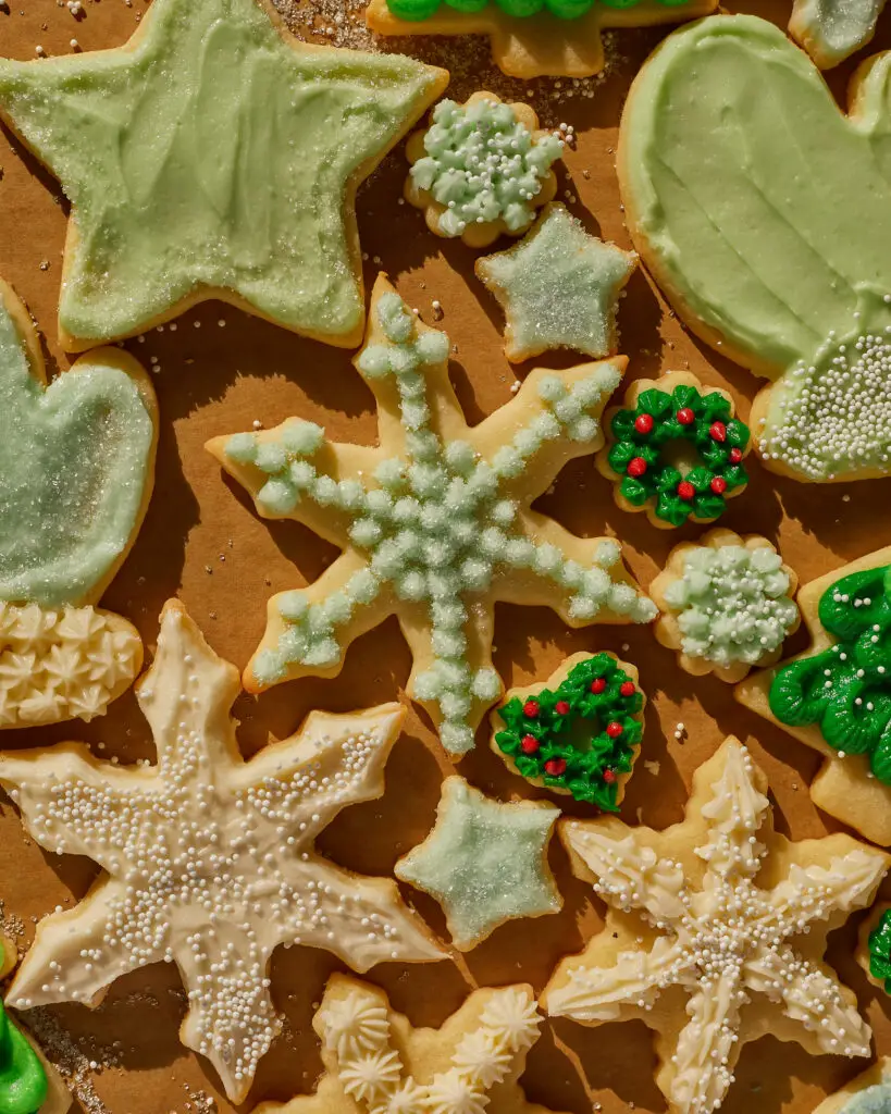 an assortment of holiday sugar cookies in snowflakes, mittens, trees stars and more, frosted with green blue and white buttercream