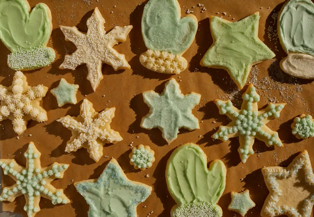 an assortment of holiday sugar cookies in snowflakes, mittens, trees stars and more, frosted with green blue and white buttercream  