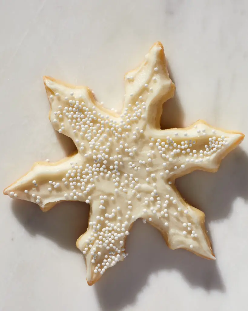 a snowflake sugar cutout cookie cookie, frosted with white buttercream and white sprinkles