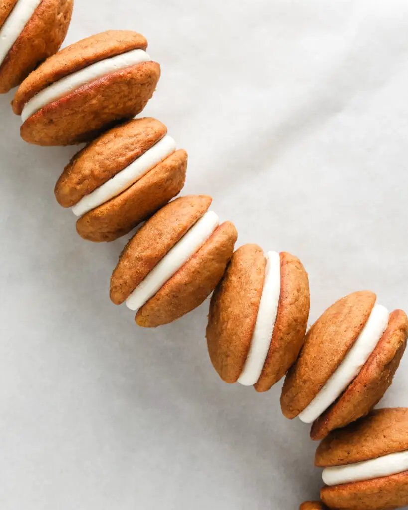 pumpkin whoopie pies with cream cheese filling stacked in a line on a marble surface