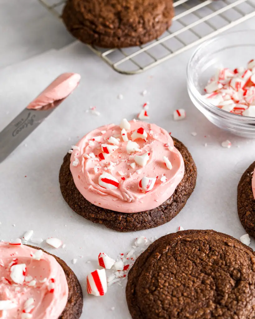 a chocolate chocolate cookie frosted with pink peppermint buttercream sprinkled with crushed up candy canes