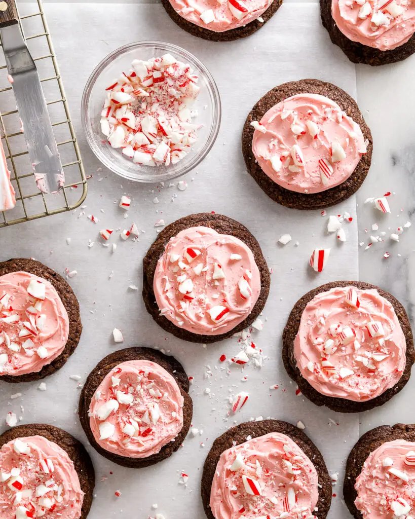 a dozen chocolate chocolate cookies frosted with pink peppermint buttercream sprinkled with crushed up candy canes