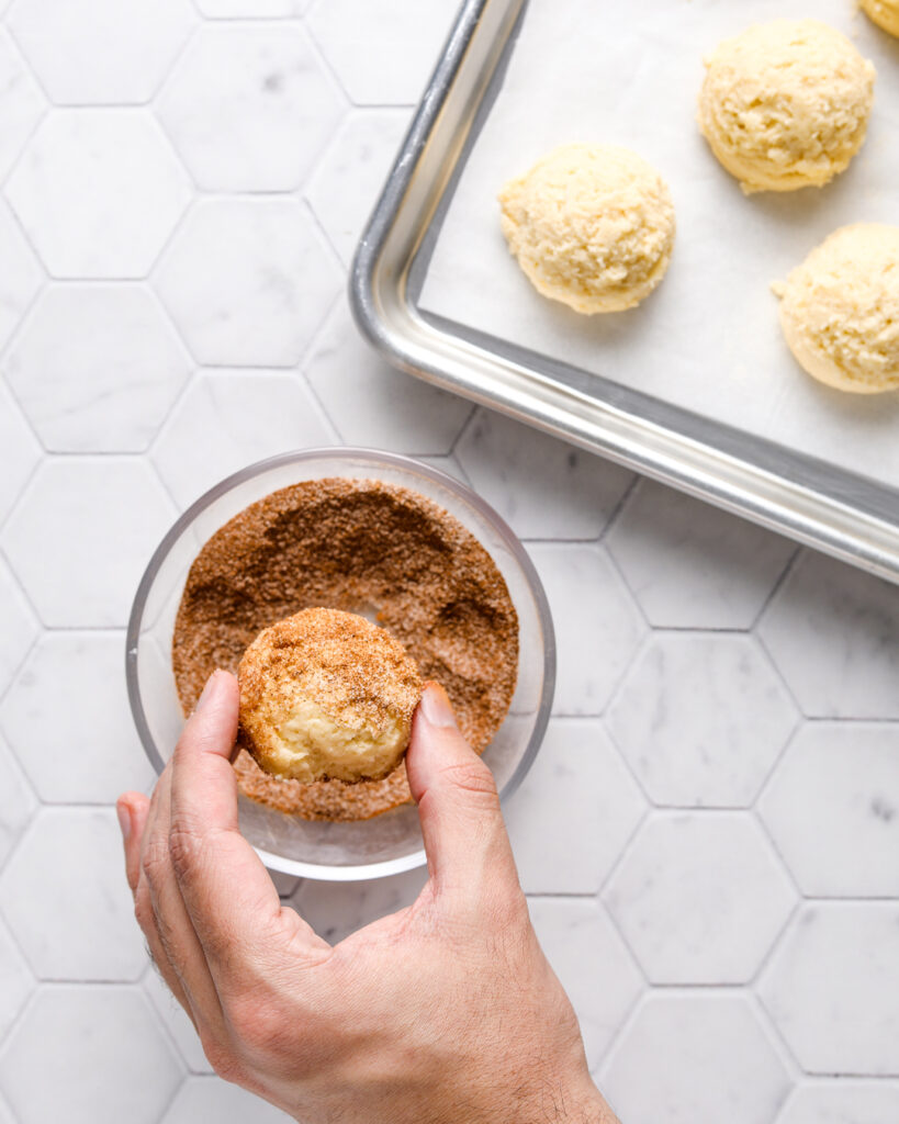 snickerdoodle cookie dough ball being dipped in cinnamon sugar