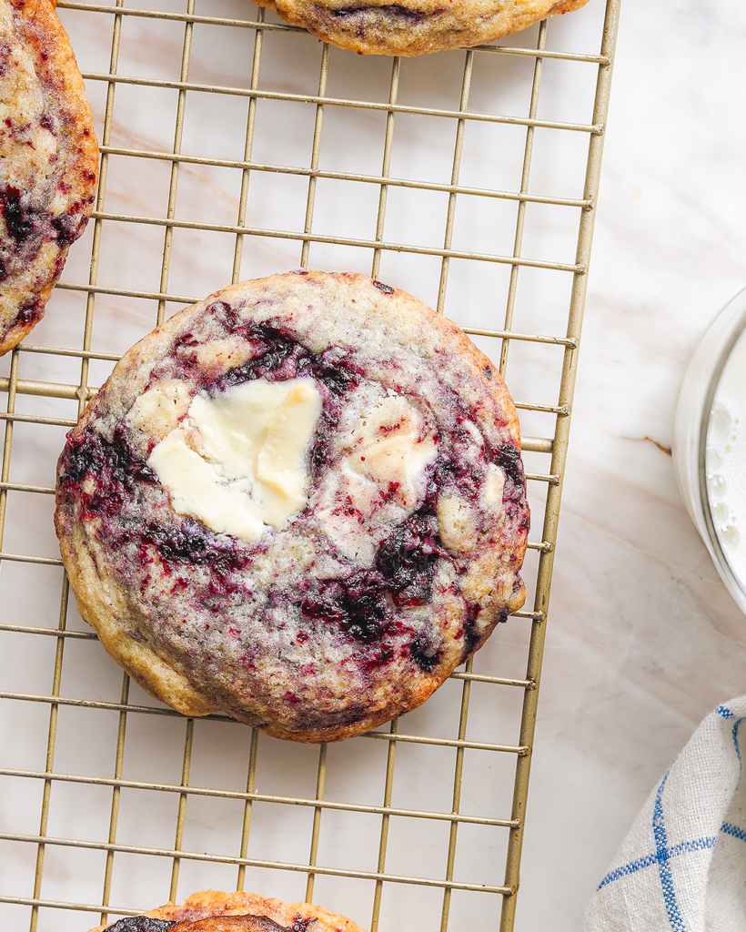 a blueberry white chocolate cookie on a cooling rack with a glass of milk off to the side