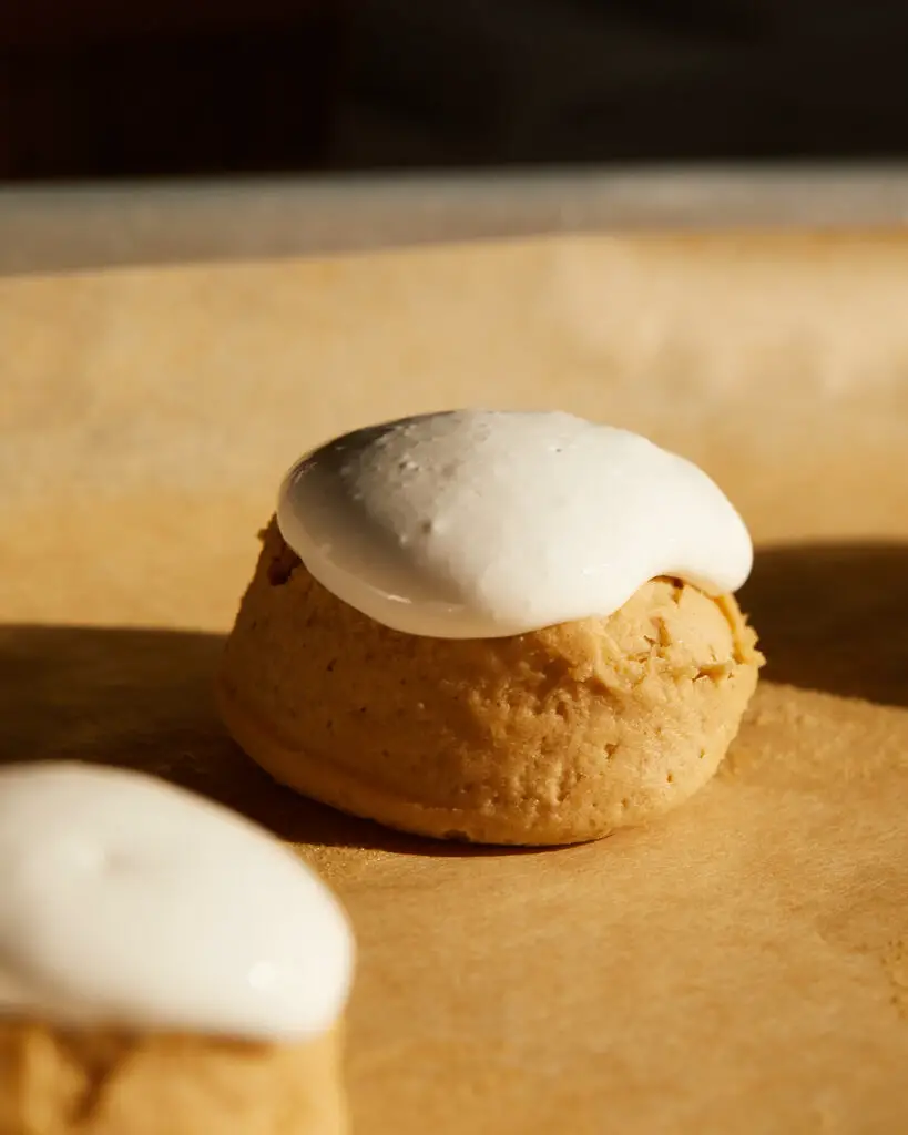 The side view of a ball of peanut butter cookie dough topped with marshmallow fluff, sitting on a baking tray