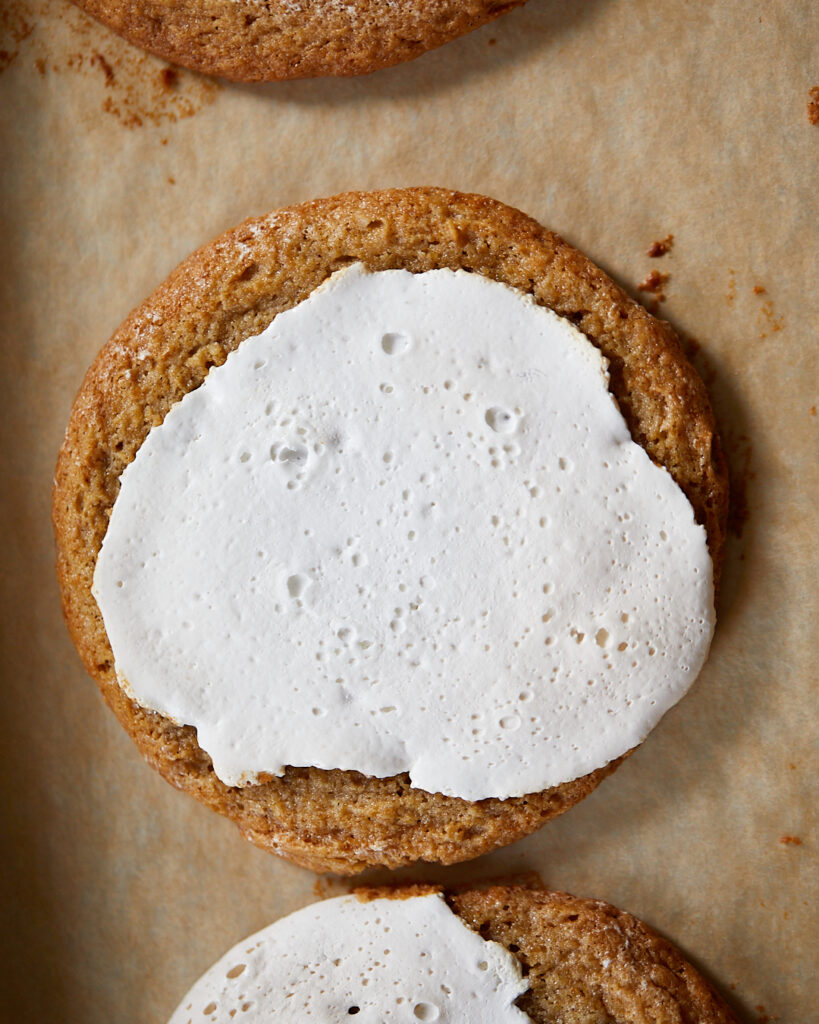 a chewy peanut butter cookie covered in toasted marshmallow fluff topping, sitting on a baking tray