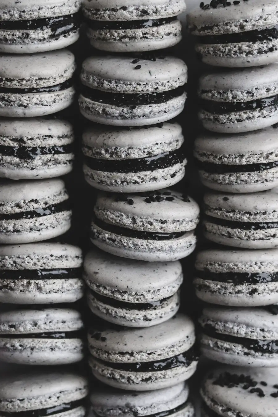 one black sesame macaron sits on its side facing up at the camera to show its black sesame honey filling