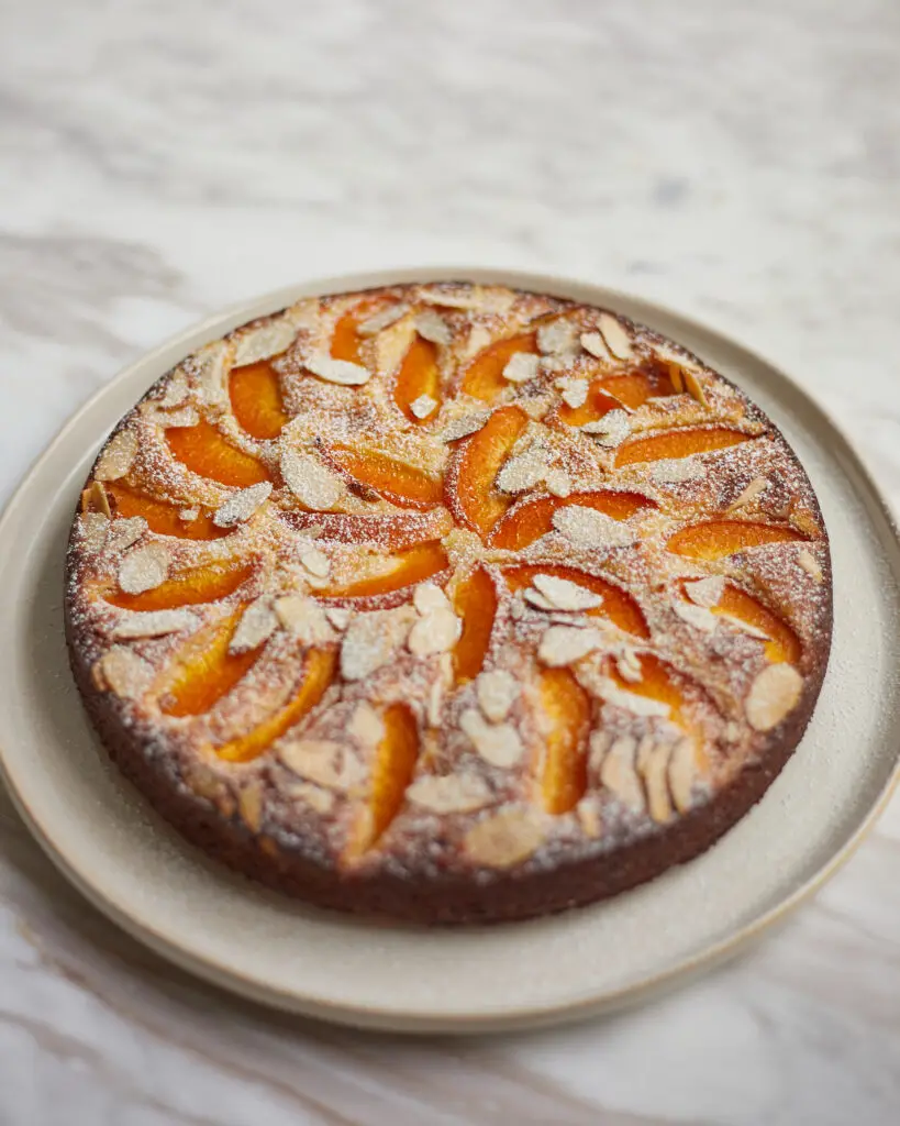 Apricot almond cake sprinkled with slivered almonds and powdered sugar on a serving plate