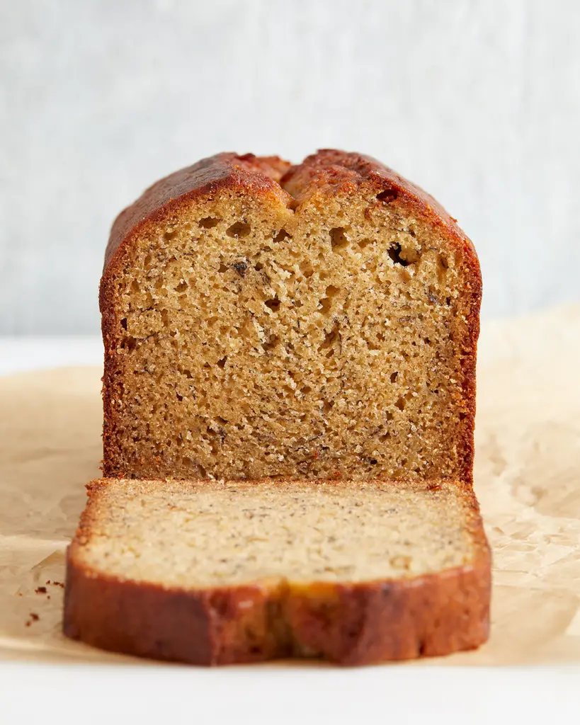 the cross-section of a loaf of banana bread with  a fallen slice in front of it