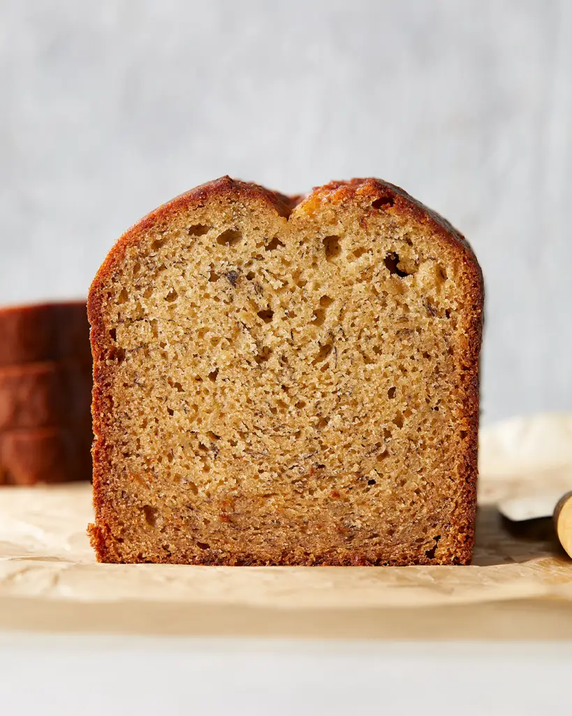 the cross-section of a loaf of banana bread with a stack of slices in the background and a small knife next to it