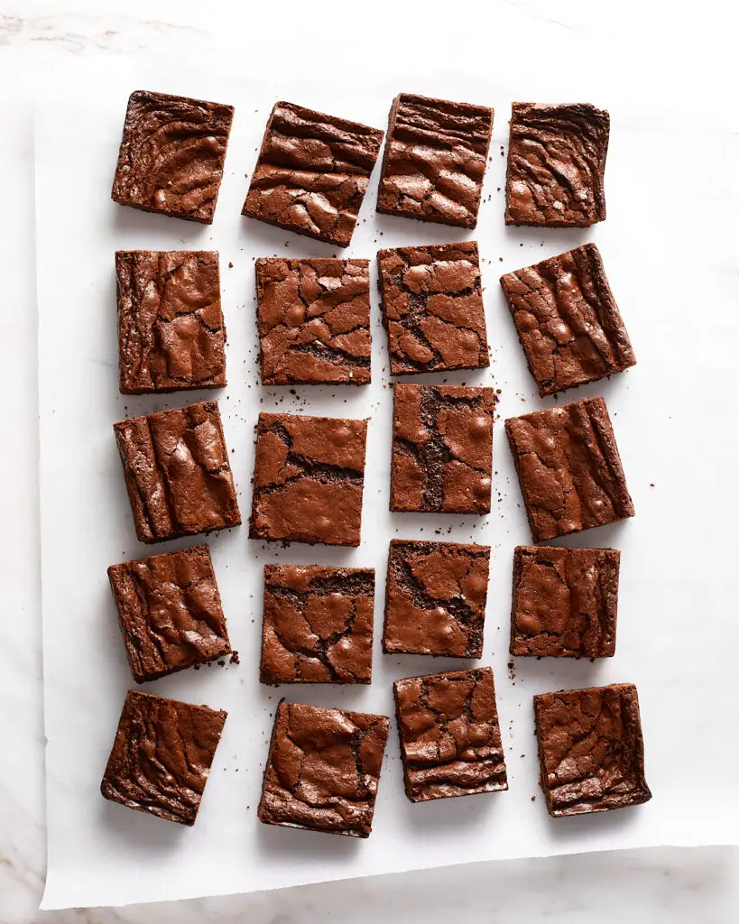 a tray of thin chewy brownies, cut into squares, placed on a white piece of parchment 