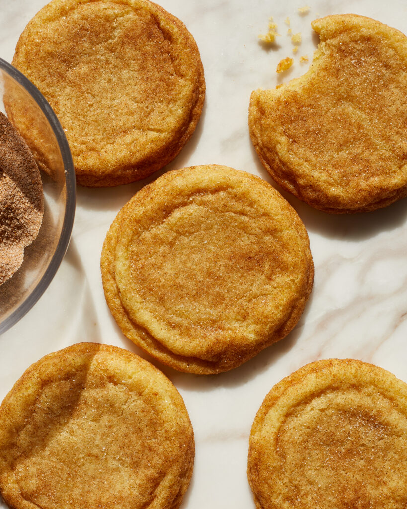 chewy snickerdoodle cookies on a white marble surface next to a bowl of cinnamon sugar