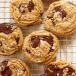 chocolate chip cookies with big puddles of chocolate and sprinkled with flakey salt on a cooling rack