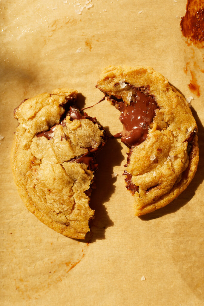 A gooey chocolate chip cookie with flakey sea salt broken in half oozing chocolate