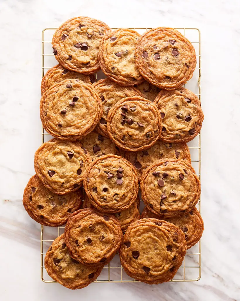 two dozen crispy brown butter chocolate chip cookies overflowing on a cooling rack