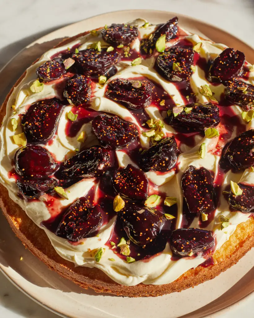 A diagonal angle of red wine pached fig cake with mascarpone whipped cream and pistachios on top