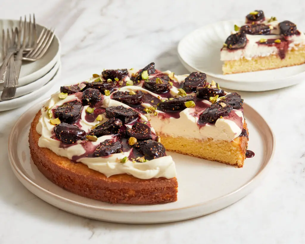 a slice is cut out of a single layer of yellow cake topped with mascarpone whipped cream and red wine poached figs
