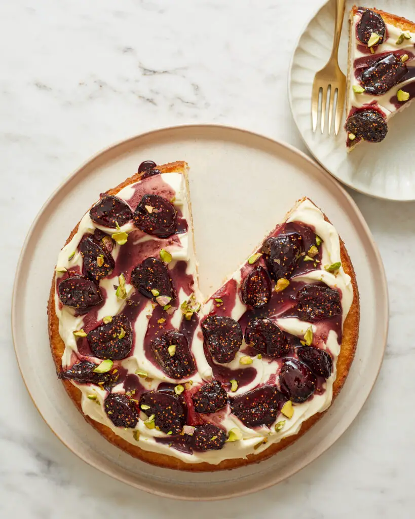 a slice is cut out of a single layer of yellow cake topped with mascarpone whipped cream and red wine poached figs