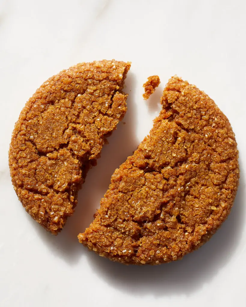 a chewy ginger molasses cookies broken in half on a white marble surface