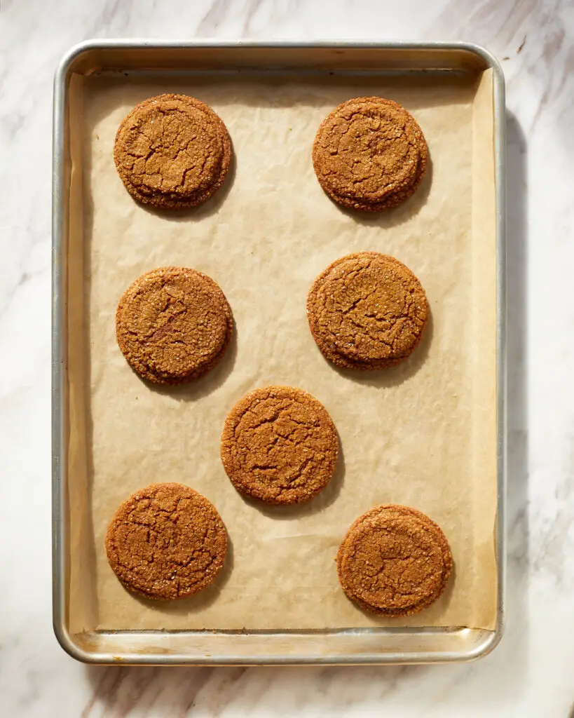 seven crinkly, chewy ginger molasses cookies with sparkly sugar coating on a baking sheet