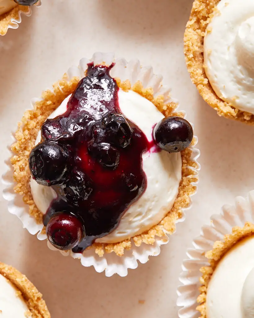 A mini no-bake cheesecake in its liner topped with a blueberry compote on a serving plate