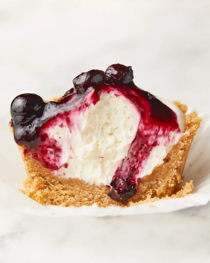 A mini no-bake cheesecake in its liner topped with a blueberry compote 