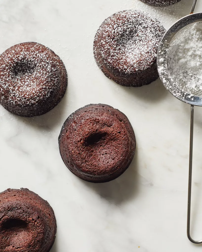 mini molten chocolate lava cakes dusted with powdered sugar with a fine mesh sieve of powdered sugar on the side