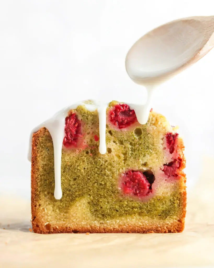The cross section of a matcha raspberry swirl pound cake loaf, with a with a wooden spoon drizzling icing over it. 