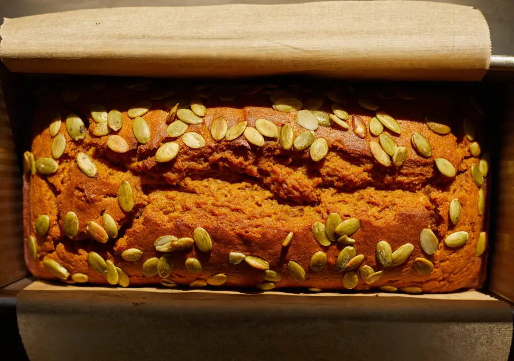 a loaf of pumpkin bread slices with pumpkin seeds or pepitas in a pullman loaf tin