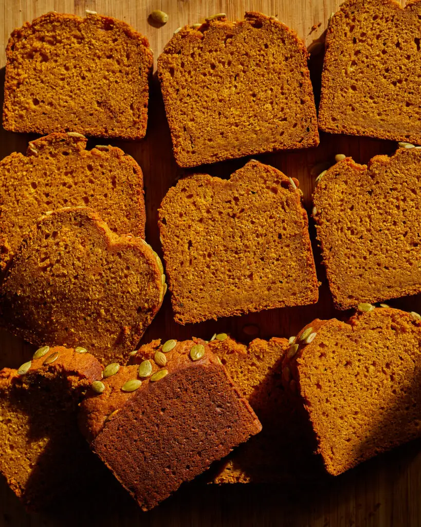 rows of pumpkin bread slices with pumpkin seeds or pepitas on top of a cutting board