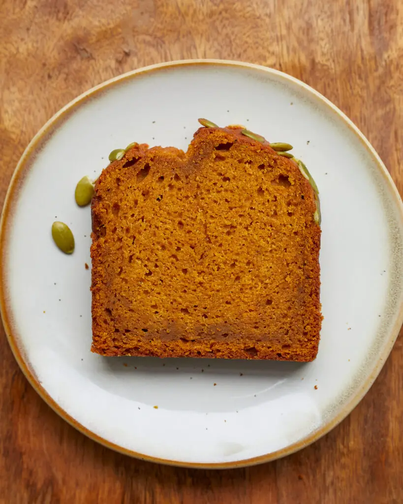 a slice of pumpkin bread with pepitas or pumpkin seeds on top on a blue dessert plate 