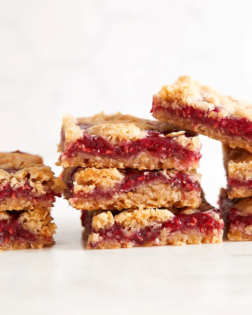 Several raspberry oat raspberry bars stacked on top of each other on a white marble countertop