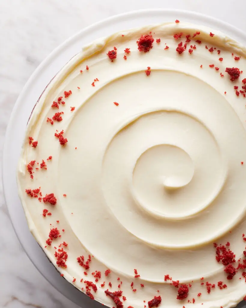 overhead view of a red velvet cake with cream cheese frosting in a swirl on top with red velvet crumbs in a circle around the top