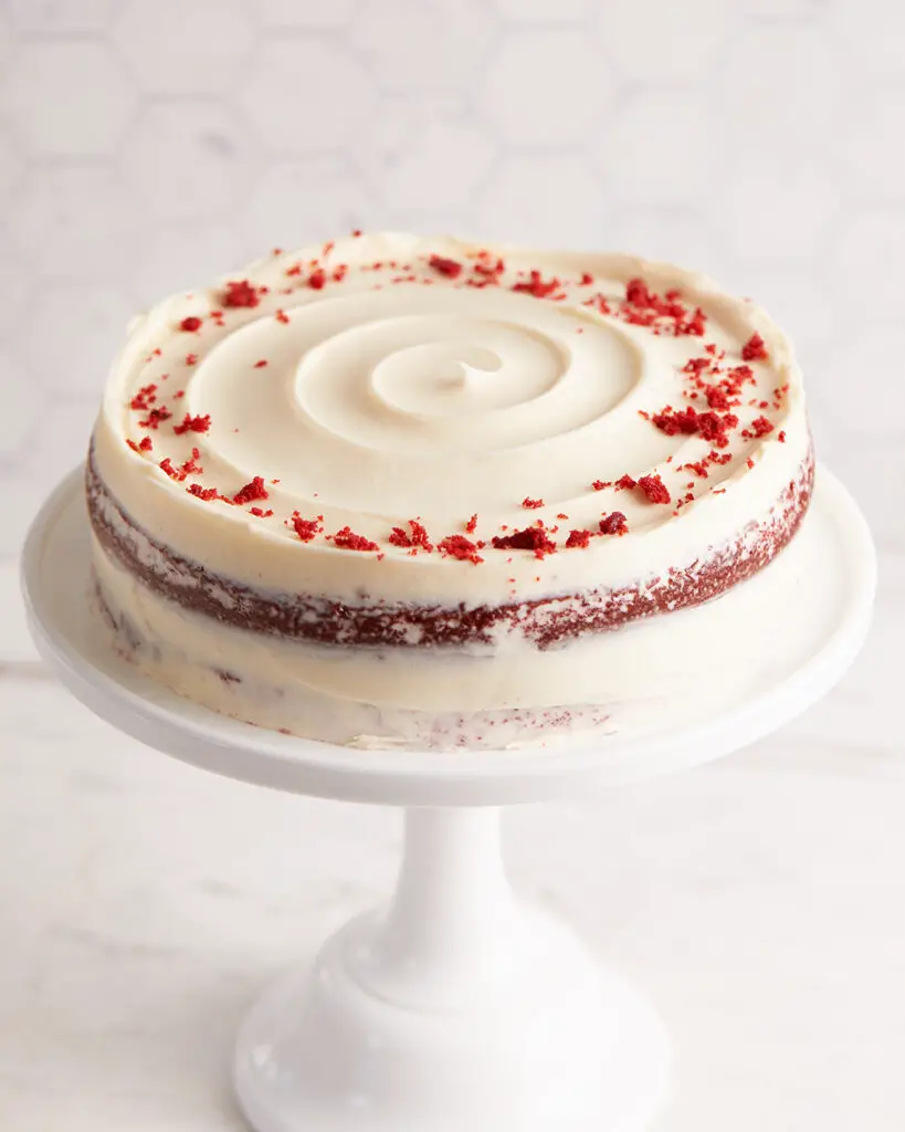 red velvet cake with cream cheese frosting in a swirl on top with red velvet crumbs in a circle around the top