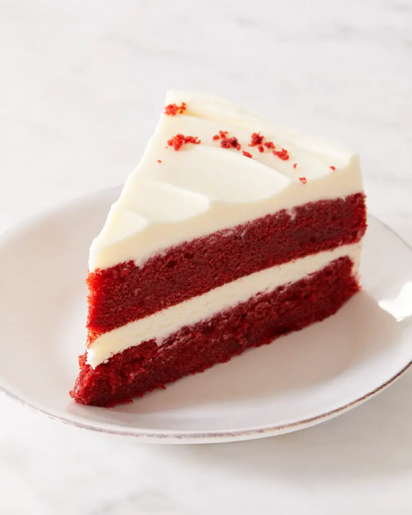 a slice of red velvet cake with cream cheese frosting on a white dessert plate on a white countertop