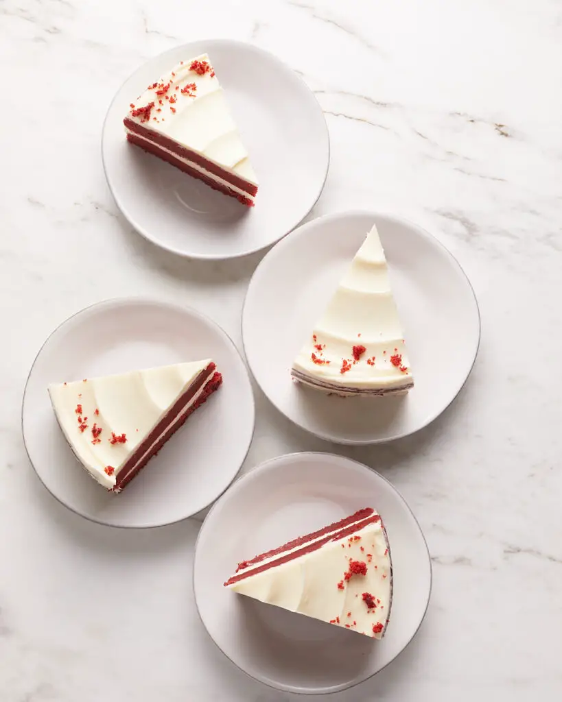 overhead view of four slices of red velvet cake with cream cheese frosting on white dessert plates