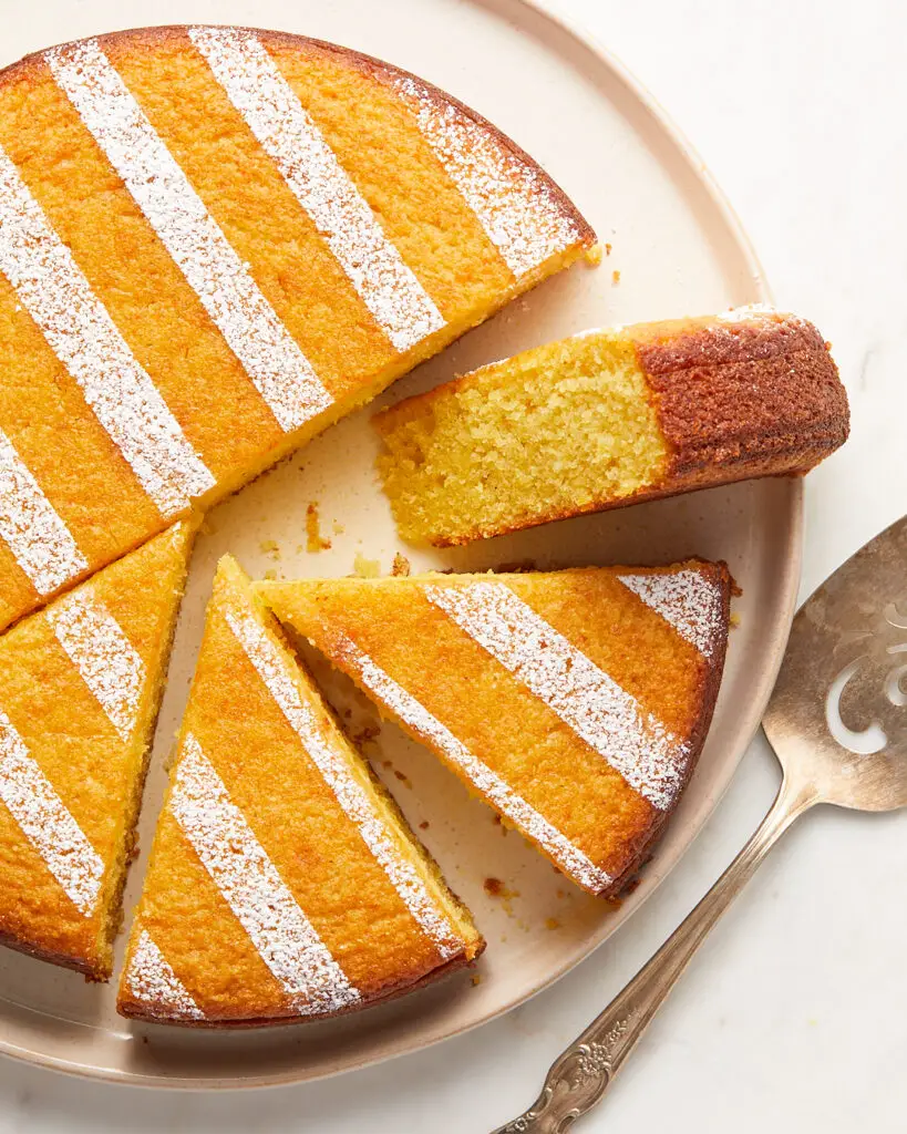 ricotta olive oil lemon snacking cake cut into sliced on a serving plate next to an antique cake server