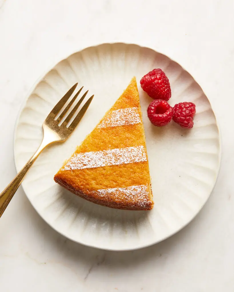 a slice of ricotta olive oil lemon snacking cake on a white dessert plate with raspberries 