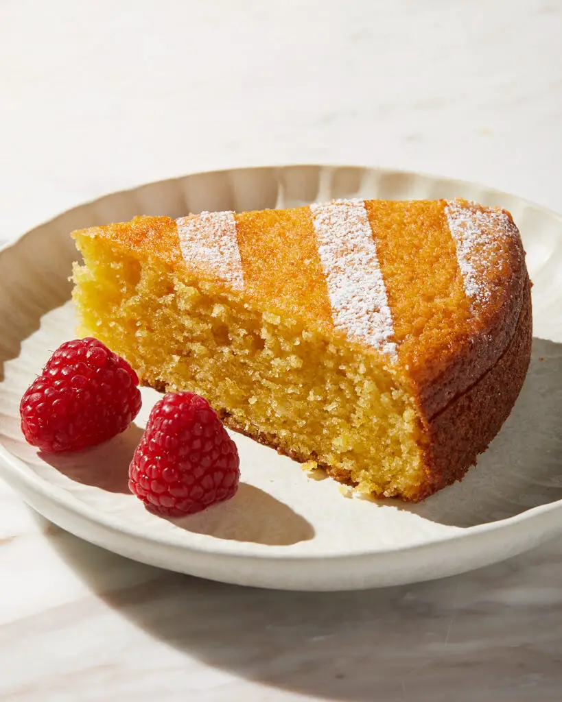 a slice of ricotta olive oil lemon snacking cake on a white dessert plate with raspberries 