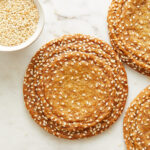 large sesame honey cookies with crinkles along the edges and a small pinch bowl of toasted sesame seeds to the side