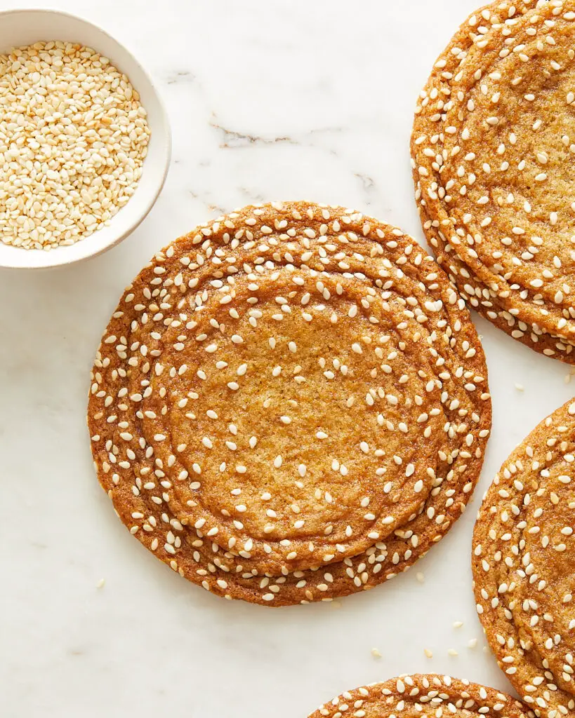 large sesame honey cookies with crinkles along the edges and a small pinch bowl of toasted sesame seeds to the side 