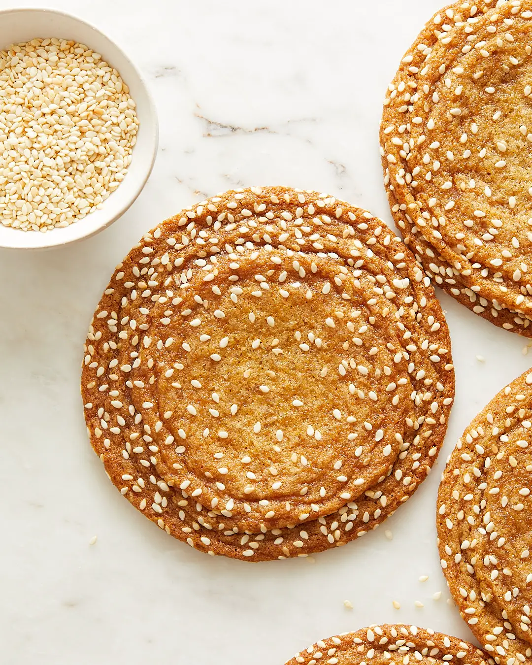 large sesame honey cookies with crinkles along the edges and a small pinch bowl of toasted sesame seeds to the side