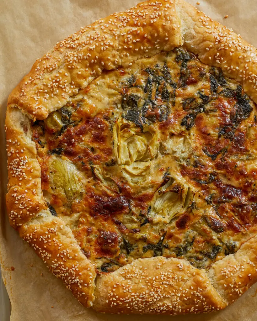 a close-up of spinach artichoke dip galette with charred cheese on top and visible half artichokes in the filling
