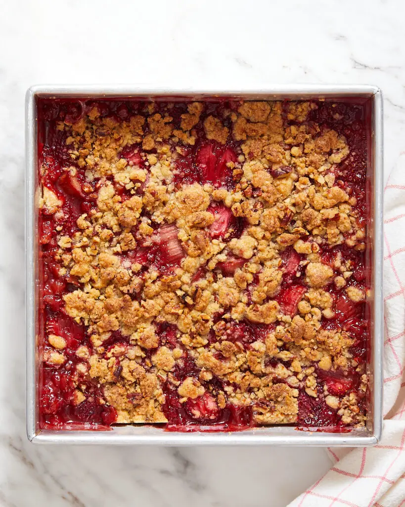 a tin of vegan strawberry rhubarb crumble with a white and red-striped towel next to it